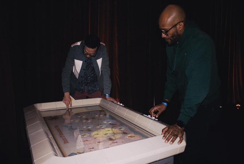 Guests standing around the rim of the backlit Broadcast Map console, working its mechanical controls together